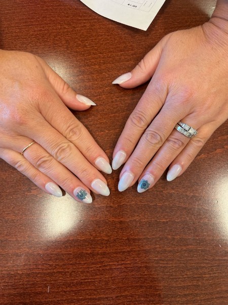 Two hands showing almond-shaped neutral nails with blue-green decorative accent designs.