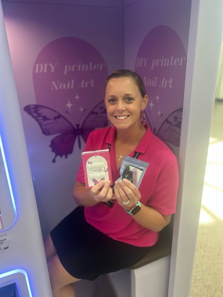 A woman seated in the Nailstar booth holding two packaged nail sets.