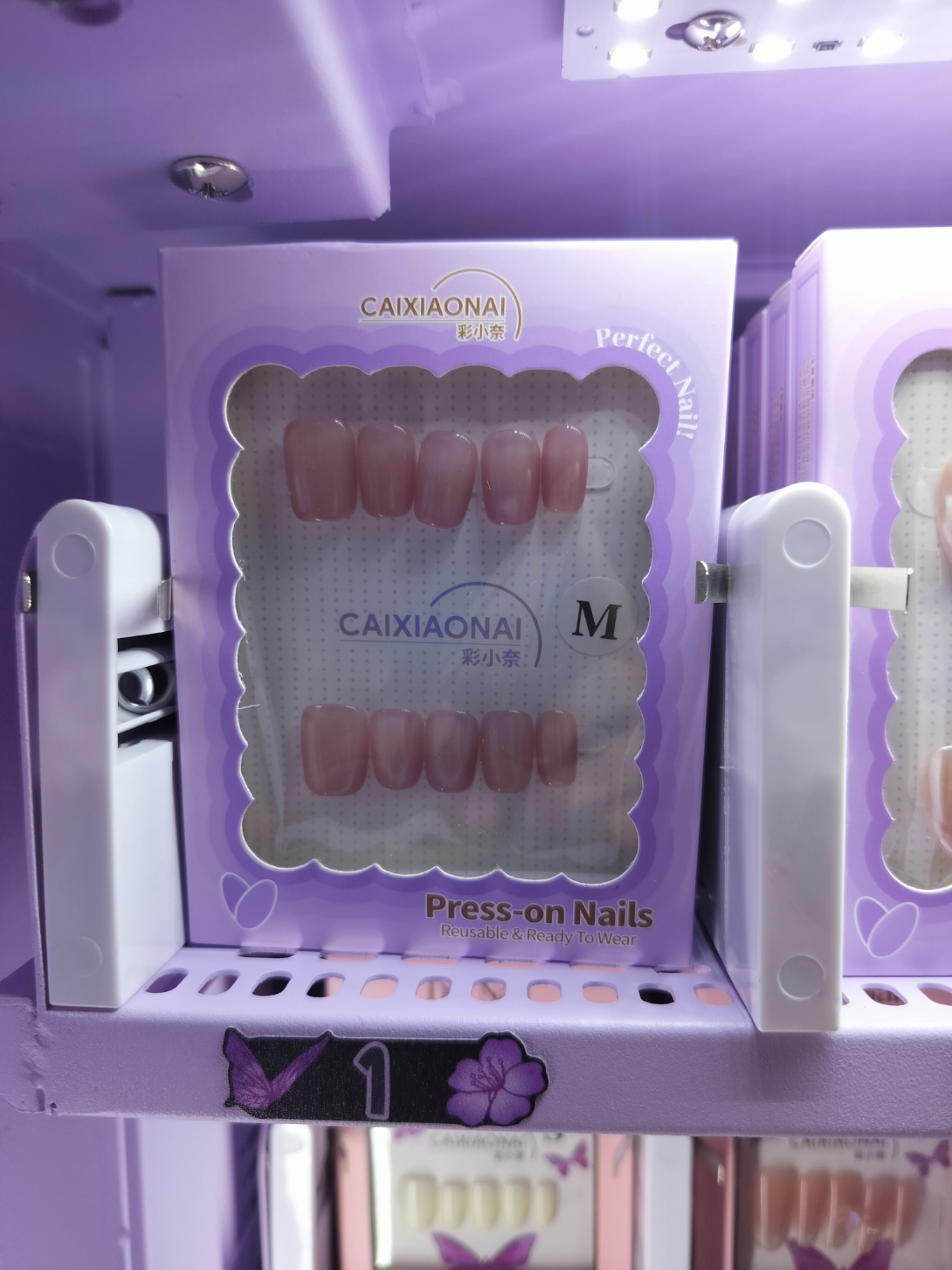 Packaged neutral pink press-on nails in a lavender display inside our vending machine.
