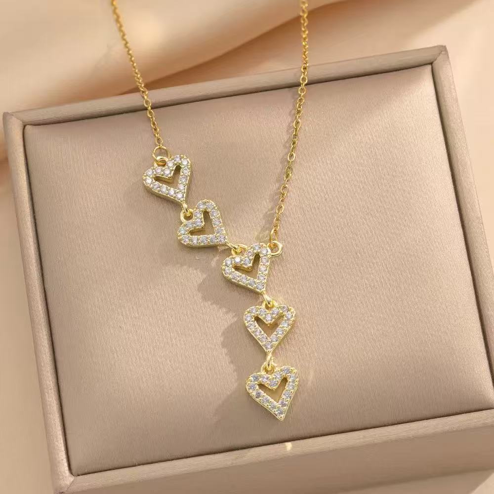 A gold-tone necklace with five open heart pendants arranged vertically on a jewelry display.