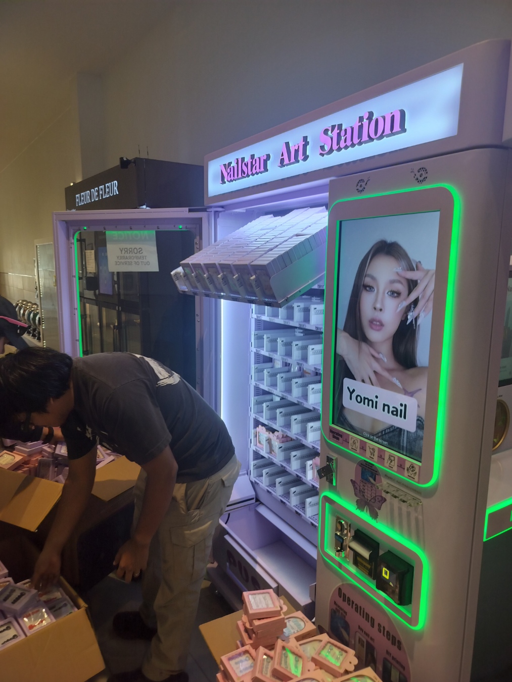 A team member arranging packaged nails beside an open lavender Nailstar vending machine.